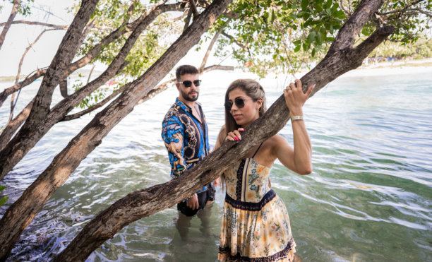 戴着太阳镜的情侣在海岸边和树木中摆姿势 - 股票照片图片下载