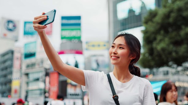 日本女性在城市中自拍微笑，与直播博主一起进行内容创作。视频、社交媒体和个人资料照片在东京，包含旅行、度假和应用程序的帖子与网站。图片下载