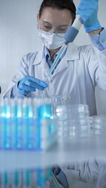 穿着实验室外套、蓝色医用手套、口罩和防护眼镜的女科学家正在现代实验室中使用微量移液器填充试管。低调照明的照片。科学与医学图片下载