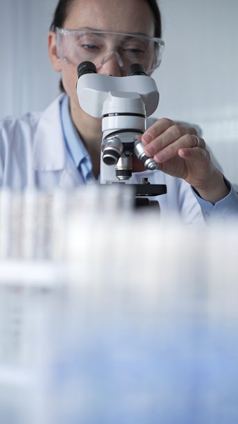 穿着实验室外套和防护眼镜的女科学家正在现代实验室中使用显微镜。低调照明的照片。科学与医学概念。图片下载