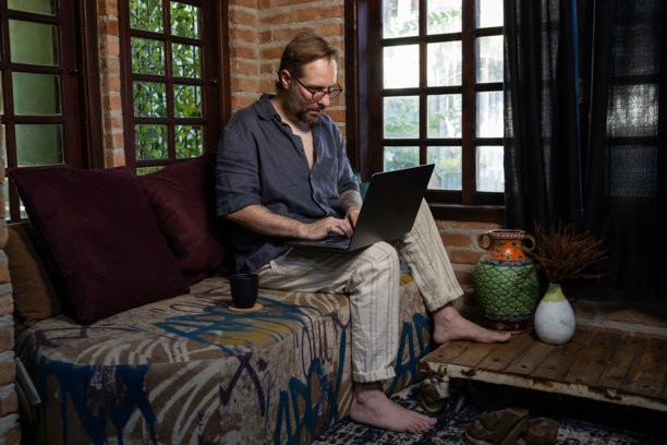 成熟男性在家沙发上使用笔记本电脑并喝咖啡的照片图片下载