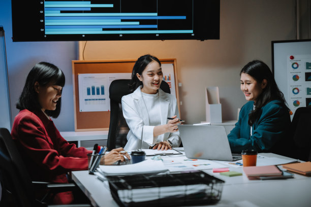 三位年轻的亚洲女商人在明亮的现代办公室中讨论一个项目，合作使用笔记本电脑，并分析显示在大屏幕上的图表和数据。图片下载