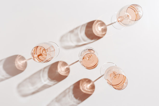 玫瑰酒杯极简风格俯视图。假日美学静物照片，自然光下的酒杯，阳光投射的阴影，米色粉色柔和色调，饮品横幅背景，留白空间。图片下载