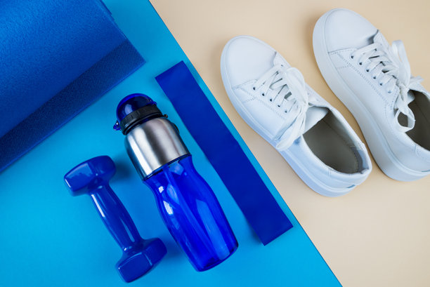 运动配件的概念。一张白色运动鞋、蓝色哑铃、蓝色瑜伽垫和其他运动器材在浅米色背景下的照片。俯视角度。图片下载