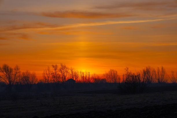 这张照片捕捉了乡村风景下令人惊叹的日落。太阳在地平线下落，天空被鲜艳的橙色和黄色染满。图片下载