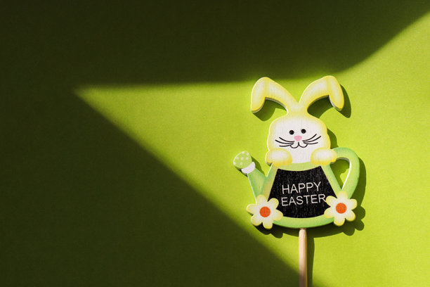 一个装饰性的复活节兔子雕像，采用木材或纸板制成，背景为明亮的绿色。兔子上写着“复活节快乐”。留有文字空间。复活节问候的照片。图片下载