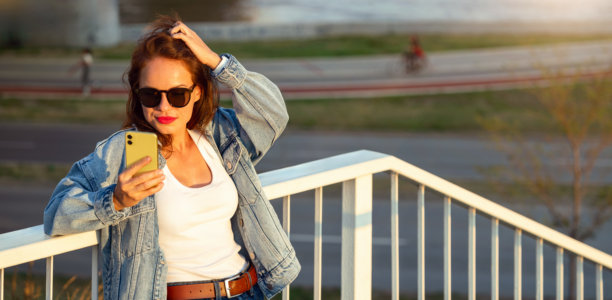 一位年轻女性穿着休闲服装，在城市环境中使用智能手机的街头风格照片。图片下载