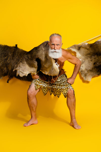 强壮的旧石器时代人类穿着豹纹皮肤的竖直全身照片，展现力量，背景为空旷的黄色。图片下载