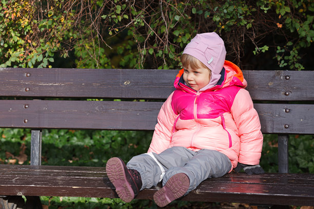 一个小女孩坐在长椅上，秋天时望向远方。横向图片。粉色和灰色的儿童秋季服装。图片下载