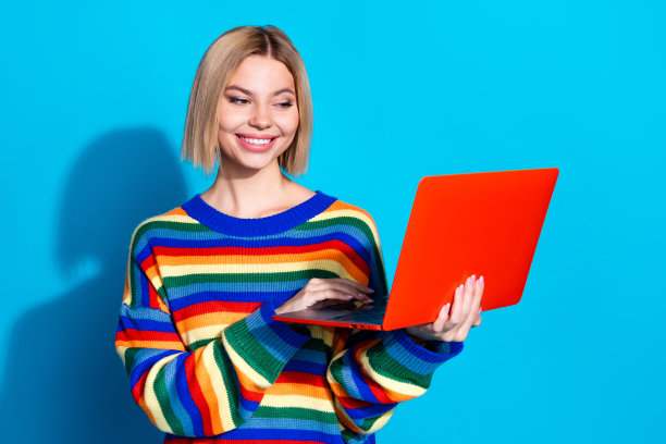 漂亮年轻女孩的照片肖像，穿着时尚条纹服装，使用笔记本电脑，背景为蓝色。图片下载