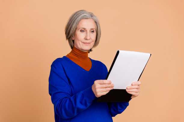 穿着时尚蓝色衣服的迷人退休女性在米色背景下阅读文件的照片肖像图片下载