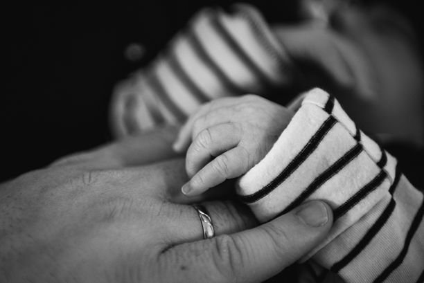 黑白照片中婴儿的手握着成年人的手指。图片下载