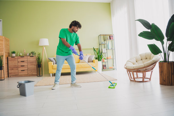 年轻男子在室内公寓的绿色环境中打扫地板，周末的全身照片图片下载