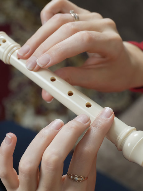 一位女性音乐家在家中练习音乐，手中演奏着白色的直笛，展示了她的技巧，身穿鲜艳的红色衬衫，手指上佩戴着戒指。竖版照片图片下载