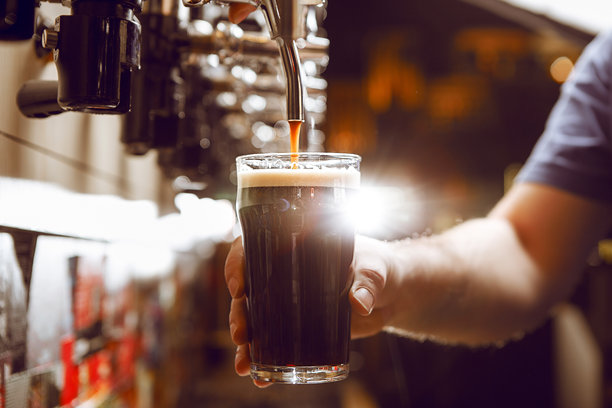 繁忙酒吧的晚上时光，黑啤酒从水龙头倒入玻璃杯的特写镜头图片下载