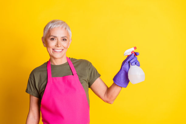 穿着粉色围裙的可爱老年女佣在黄色背景下喷洒空旷空间的照片图片下载