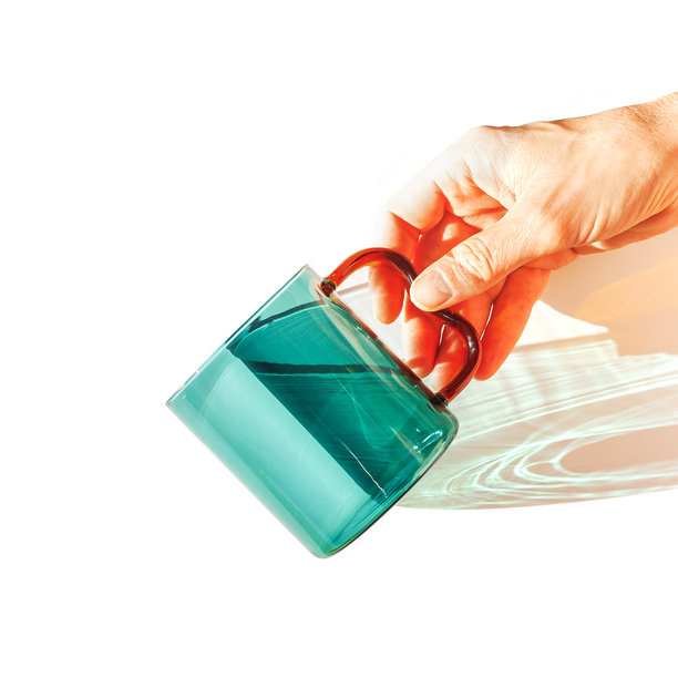 现代玻璃杯与明亮的阳光阴影，透明绿色玻璃杯的极简照片。白色背景上的金色光线反射和阴影，生活方式设计，家居装饰。图片下载