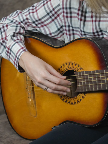 女性的手特写，熟练地弹奏着原声吉他，坐在家中的沙发上，穿着休闲服，完全沉浸在音乐的快乐中。竖版照片图片下载