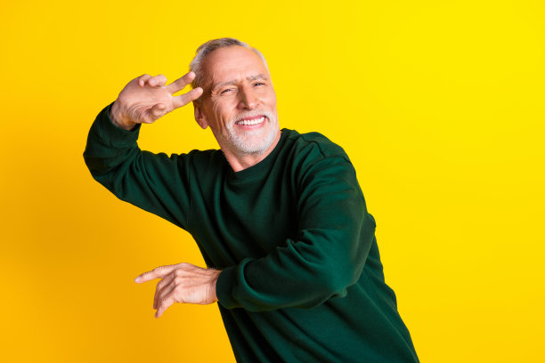 时尚的退休男士在黄色背景下穿着时尚的绿色服装，享受音乐舞蹈的肖像照片图片下载