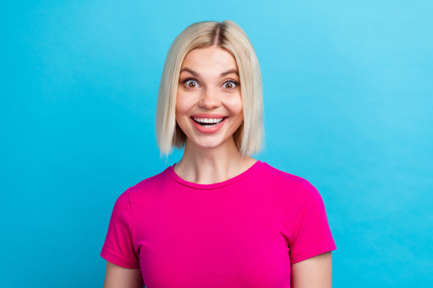 可爱年轻女士的照片肖像，兴奋地微笑，穿着时尚的粉色衣服，背景为蓝色。图片下载