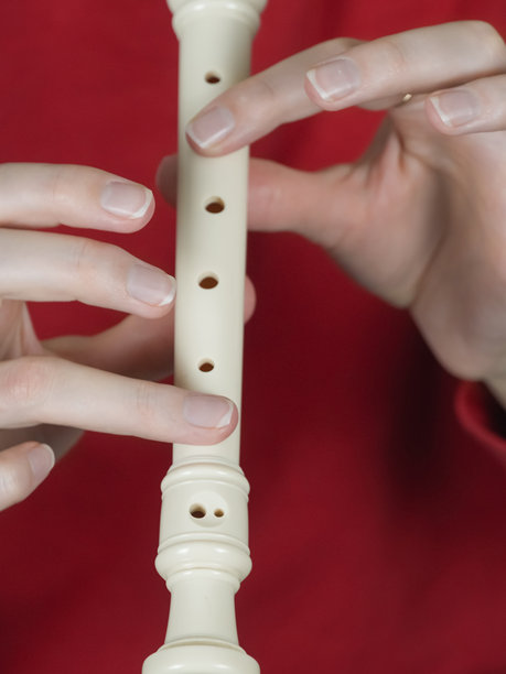 特写镜头展示音乐家手中演奏白色直笛的细节，背景为鲜艳的红色，突显出音乐表达所需的精细指法。竖版照片图片下载