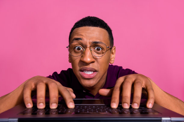 年轻男士穿着时尚的紫色服装，在粉色背景下紧张地在电脑键盘上打字的照片肖像图片下载