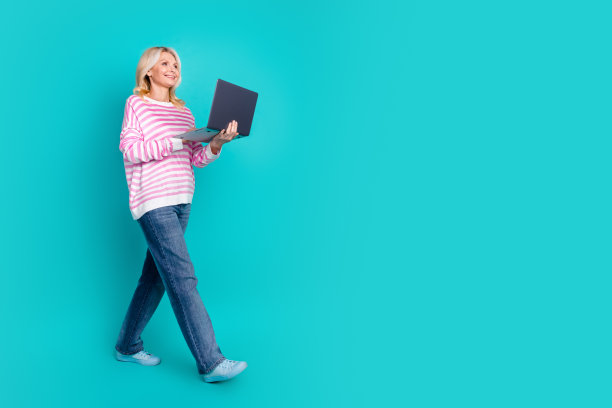 全身照片，积极的人穿着条纹毛衣，手持笔记本电脑，注视着空旷的空间，背景为蓝色。图片下载