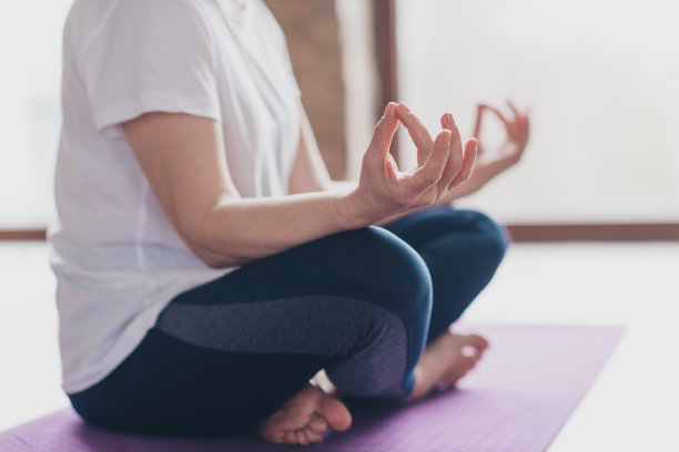 修剪过的照片，展示了一位优雅的退休女性在现代公寓的客厅中以莲花坐姿冥想，穿着运动服，体现健康的生活方式和锻炼。图片下载