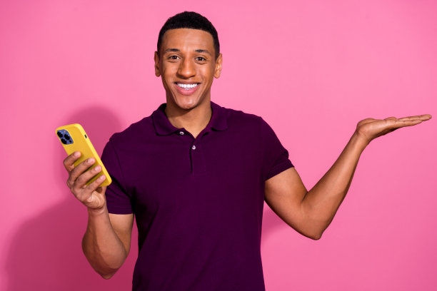 吸引人的年轻男子在粉色背景下穿着时尚的紫色衣服，手持设备，面向空白空间的照片肖像图片下载