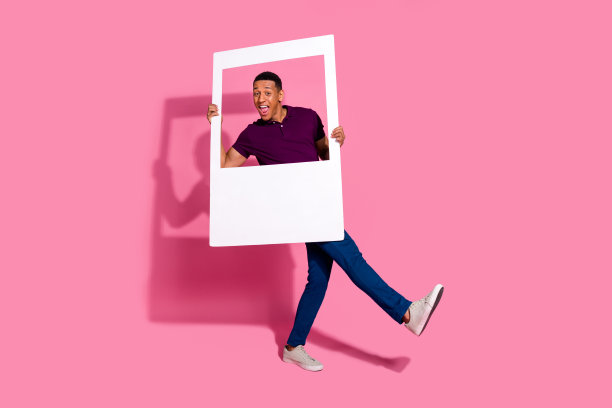 全身照，吸引人的年轻男子穿着时尚的紫色衣服，手持即时照片框，背景为粉色。图片下载