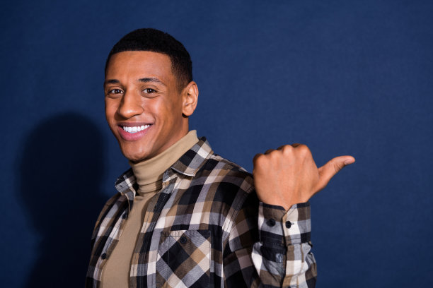 年轻男子的照片肖像，指向空白处，穿着时尚的格子服装，背景为深蓝色。图片下载