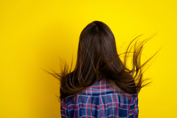 穿着时尚格子衣服的迷人年轻女性在黄色背景下摆动头发的照片肖像图片下载