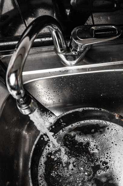 单色照片，展示一只正在流动的水龙头。干净的水流在黑暗背景下，突显细节。图片下载