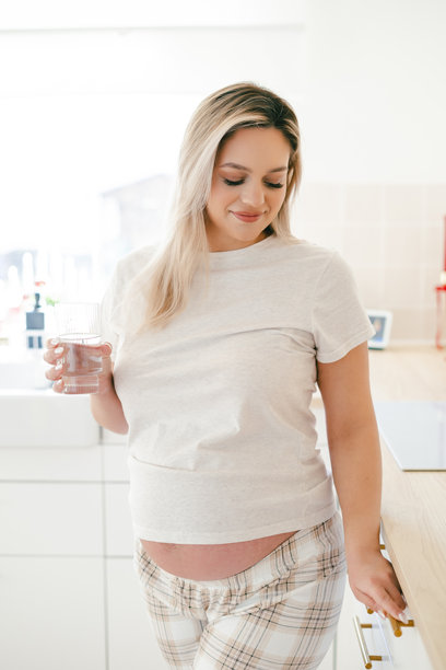 年轻漂亮的孕妇在家厨房喝水。图片下载