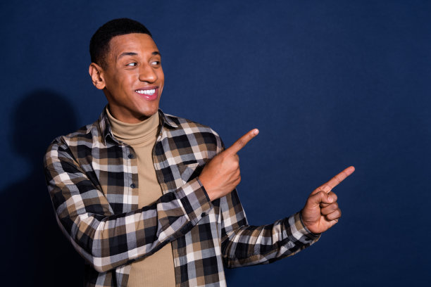 年轻男子的照片肖像，穿着时尚的格子服装，指向空旷的空间，背景为深蓝色。图片下载