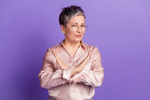 可爱的老年女士触摸眼镜，身穿时尚的缎面服装，独自站在紫色背景前的照片肖像图片下载
