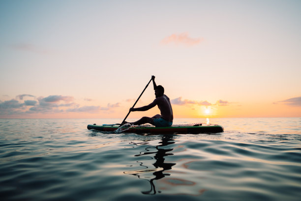 一名男子在海上日落时划着立式划水板。高质量照片图片下载