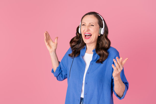 穿着时尚蓝色服装的可爱退休女性在粉色背景下戴着耳机大声呼喊的照片肖像图片下载