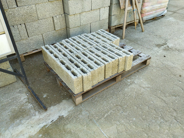 这张照片展示了户外木托盘上堆放的混凝土块。这些块是灰色的，具有特征性的孔洞，类似于煤渣砖。图片下载