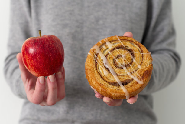 女人手持苹果和肉桂卷 健康与不健康饮食的概念照片平衡图片下载