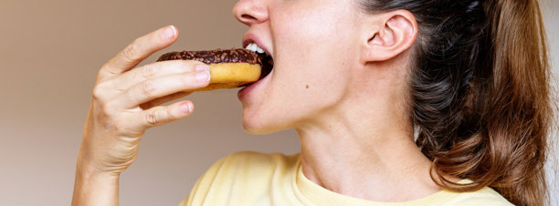 侧面照片中的女人正在吃巧克力甜甜圈图片下载