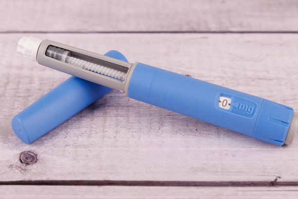 这张照片展示了一支塞马鲁肽注射笔及其包装盒，放在一张白色涂漆的木桌上，象征着健康和医疗护理。图片下载