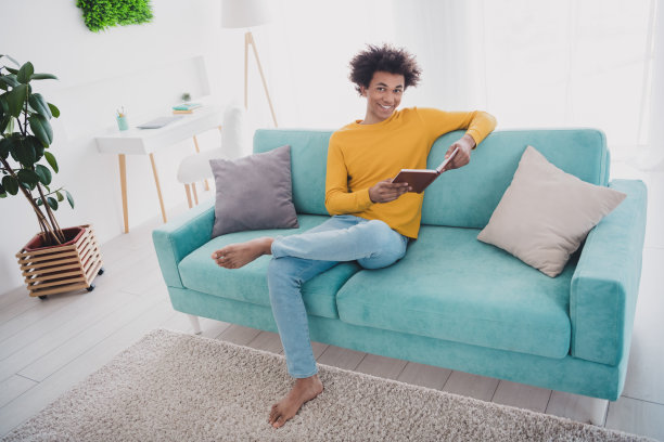 年轻男子在室内公寓里穿着黄色毛衣，悠闲地阅读一本书的全身照片图片下载