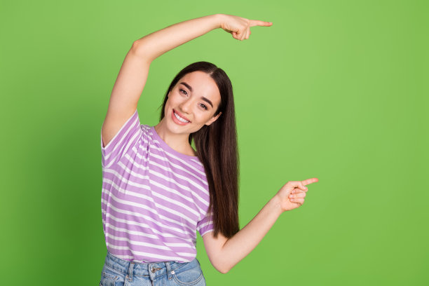 可爱的年轻女士在绿色背景下穿着时尚的紫色条纹服装，指向空白处的照片肖像图片下载