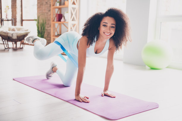 全身照片，年轻女性穿着运动服在室内健身房的垫子上拉伸腿部。图片下载