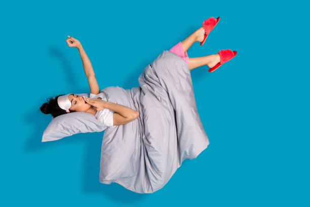 全身照片，年轻女性打哈欠、伸展，穿着睡衣，漂浮在蓝色背景上。图片下载