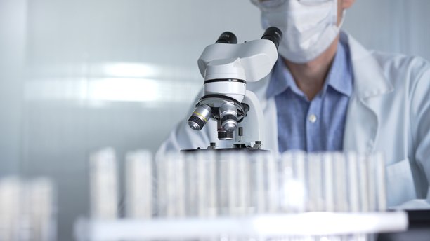 穿着白色手套、护目镜和医用口罩的男性科学家研究员正在现代实验室中使用显微镜，肖像视图。低调照明照片。科学与医学图片下载