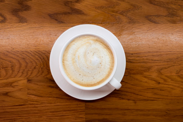 咖啡，俯视木桌或咖啡馆背景上的卡布奇诺咖啡杯，带有拉花艺术。近距离从上方拍摄的杯子，泡沫拿铁。意大利饮品。高质量照片。图片下载