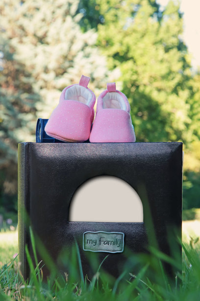 家庭相册特写，带有空白白框以便放置照片或文字。美丽的构图，草地上放着一双新生儿鞋子和一本摄影书。父母节。图片下载