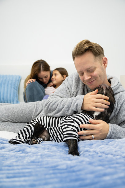 一张垂直照片，展现了一个温馨的家庭时刻，一名男子穿着条纹毛衣，正在抚摸一只狗。图片下载